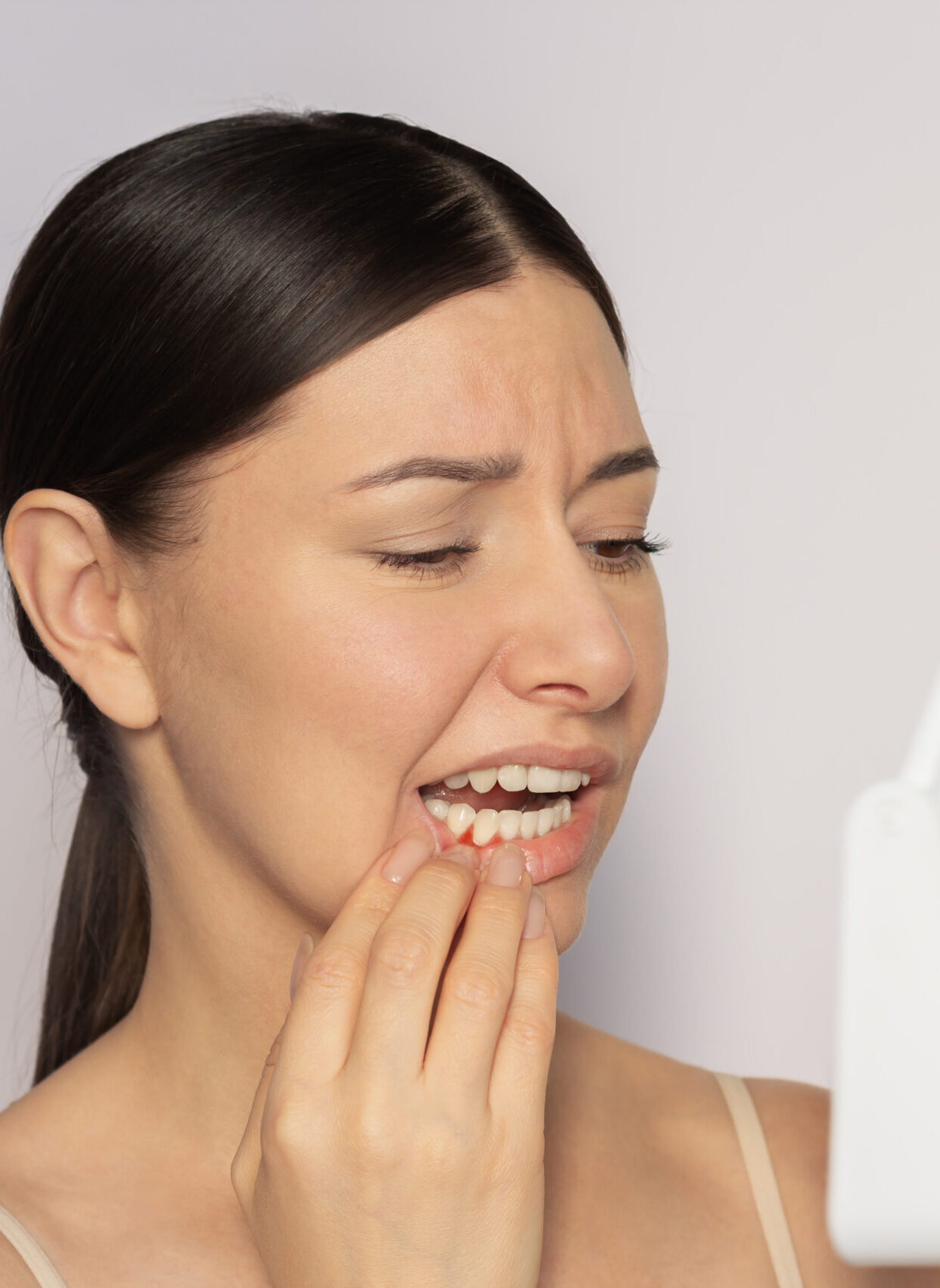 Young pretty caucasian woman looking at her red gums on her lower jaw in the mirror. She suffering from gingivitis, gum inflammation. Dental care. Dentistry. Oral care