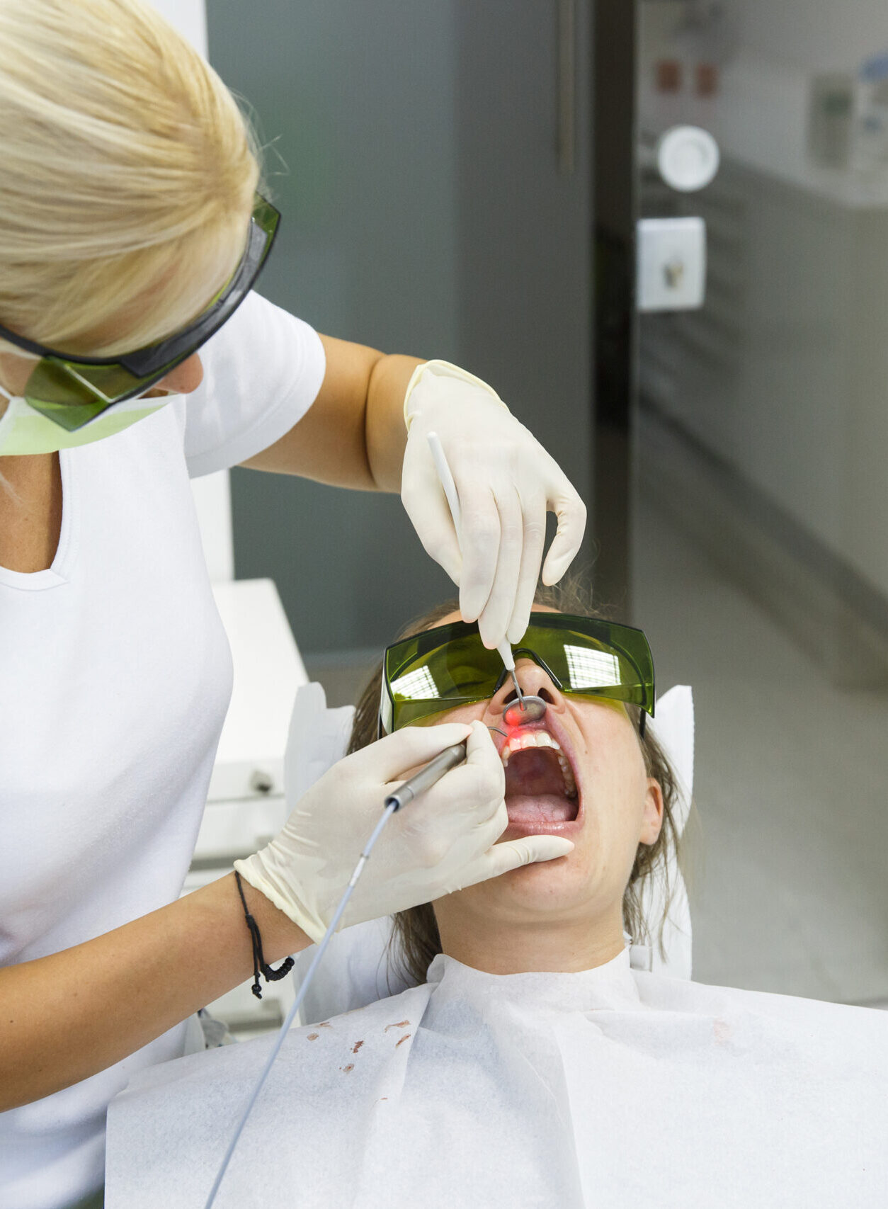 Dentist using a modern diode dental laser for periodontal care. Both wearing protective glasses, preventing eyesight damage. Periodontitis, dental hygiene, preventive procedures concept.