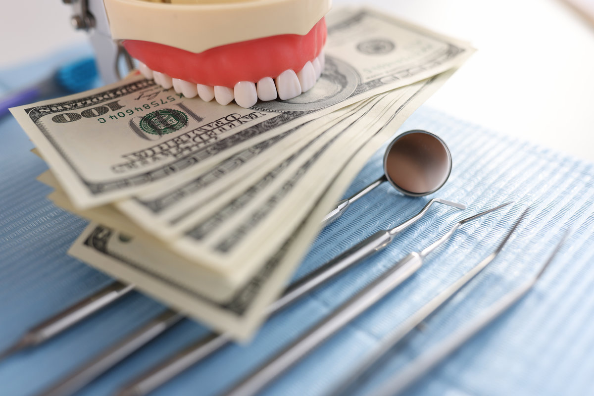 Dental artificial jaw instrument and one hundred dollar bills on dentist desk. Dental treatment cost concept