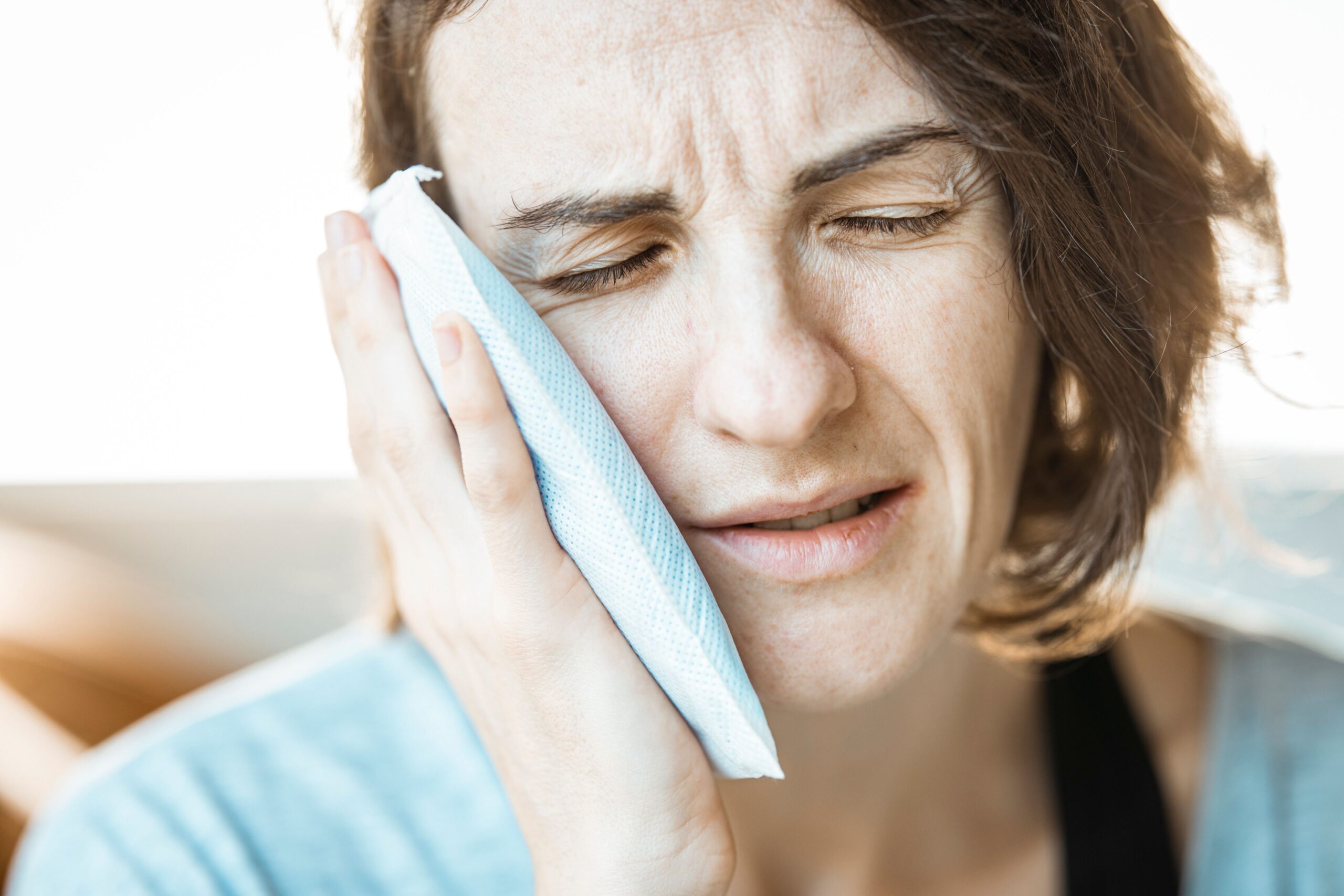 Adult woman applying cold compress to cheek for toothache relief before seeing dentist in Reno