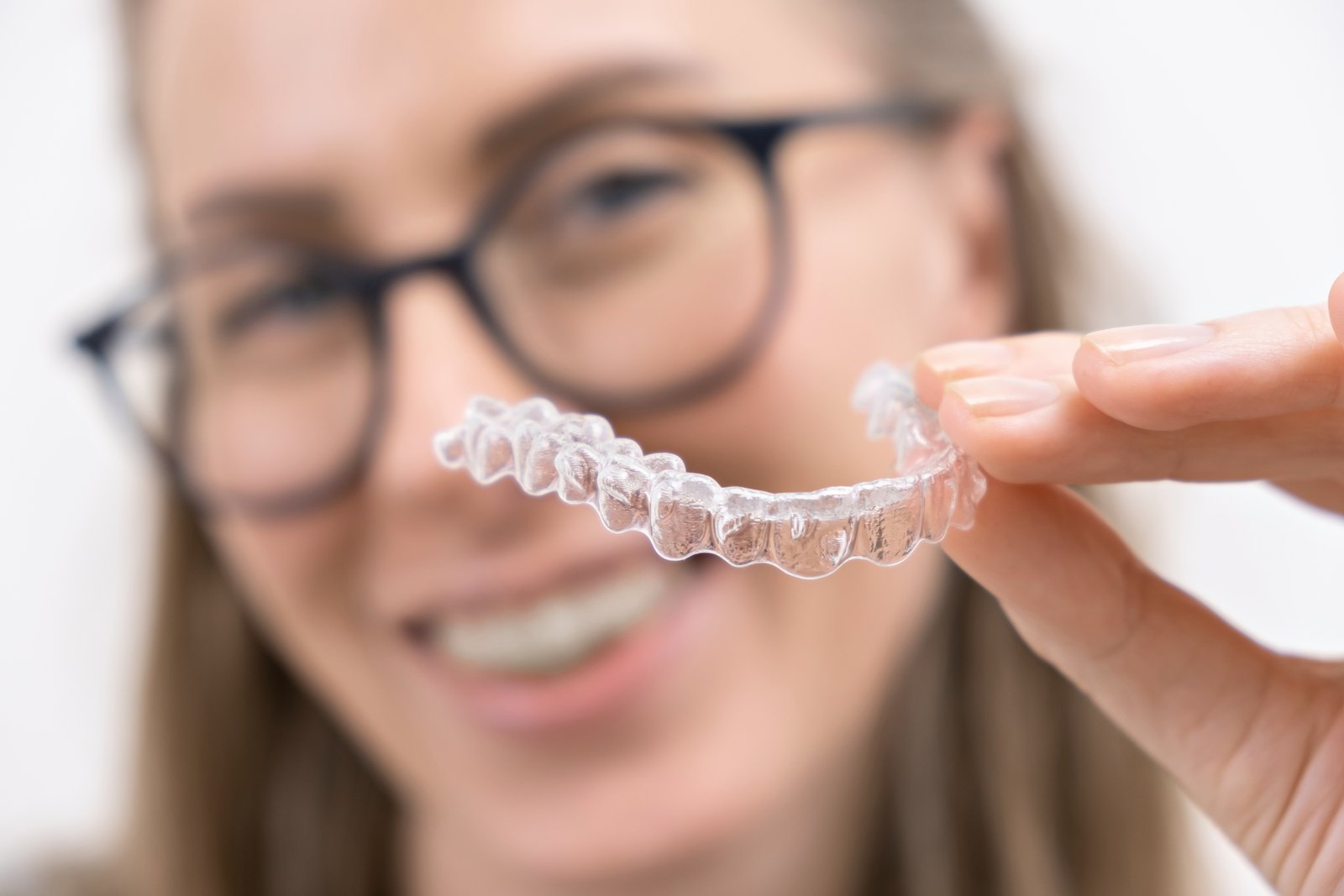Woman smiling while using a clear Invisalign aligner tray for straighter teeth and healthier gums